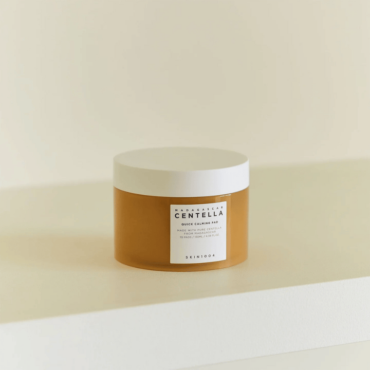 SKIN1004 Madagascar Centella Quick Calming Pad placerad på vit hylla – bärnstensfärgad burk med vitt lock och tydlig etikett framtill.