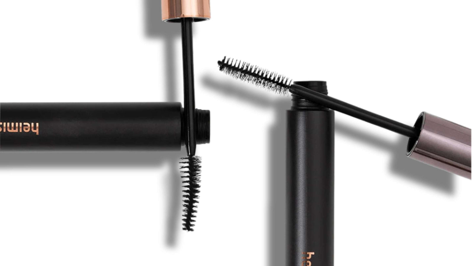 Två öppna mascaror med svarta borstar och eleganta förpackningar i metalliska färger ligger på en vit bakgrund. En mascara har en roséguldfärgad hylsa och den andra har en mattsvart design med märket "heimish" tryckt i guld.