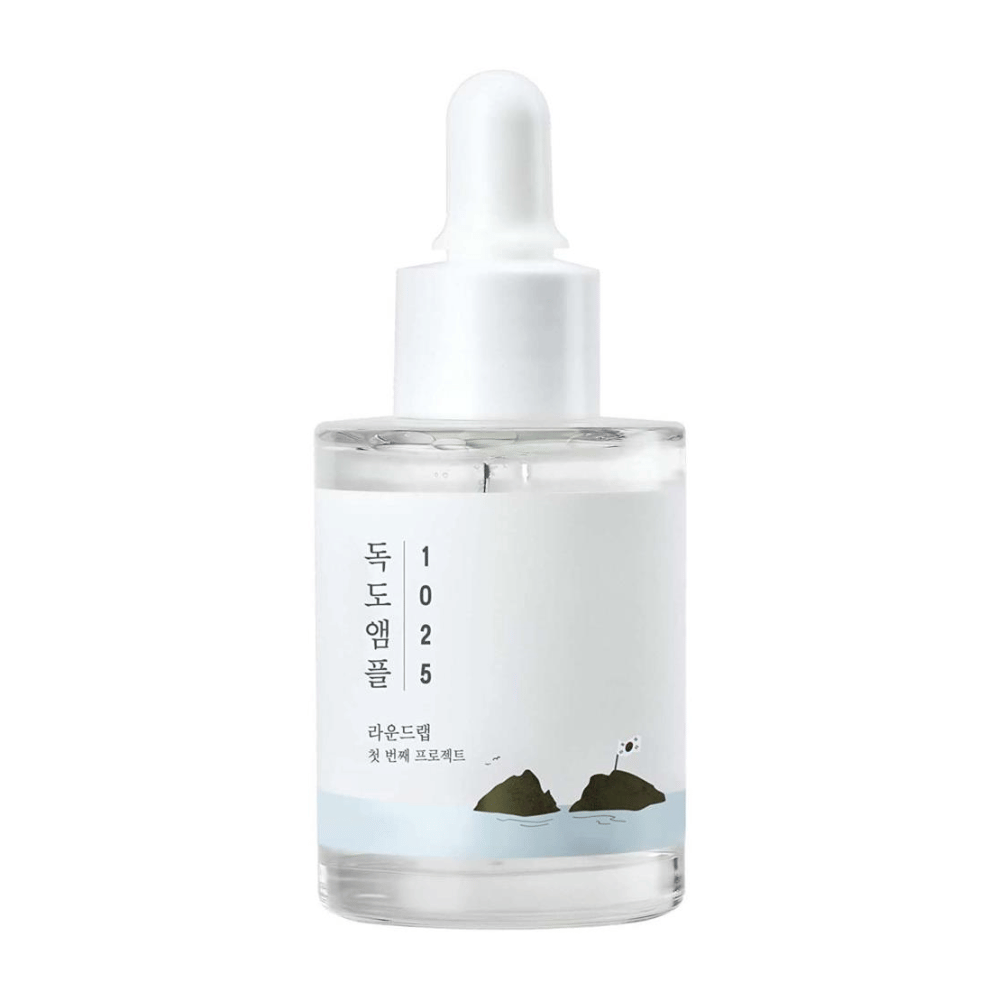 Eine durchsichtige Flasche mit 1025 Dokdo Ampoule Gesichtsserum, dekoriert mit einem minimalistischen Meeresthema, auf weißem Hintergrund.