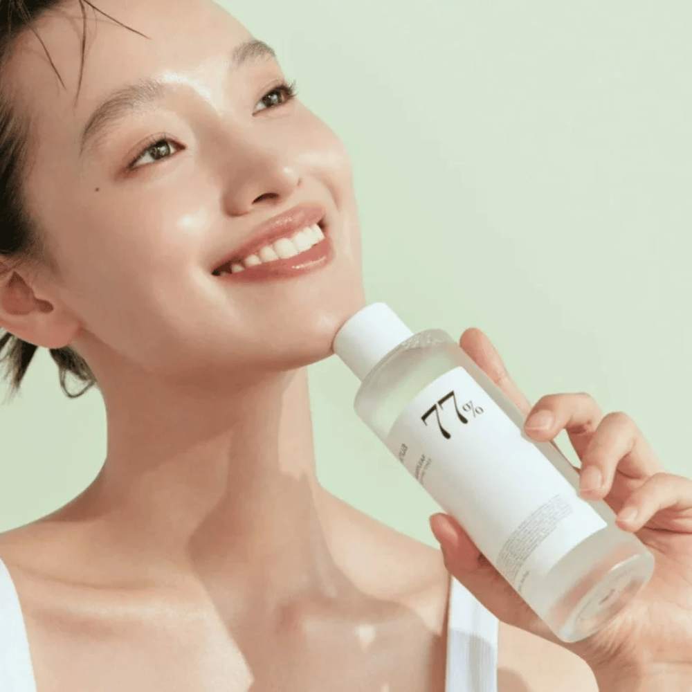 Eine Frau beruhigt ihre empfindliche Haut mit einer Flasche Heartleaf 77% Soothing Toner von Anua, die Extrakt aus Chamäleonblättern enthält.