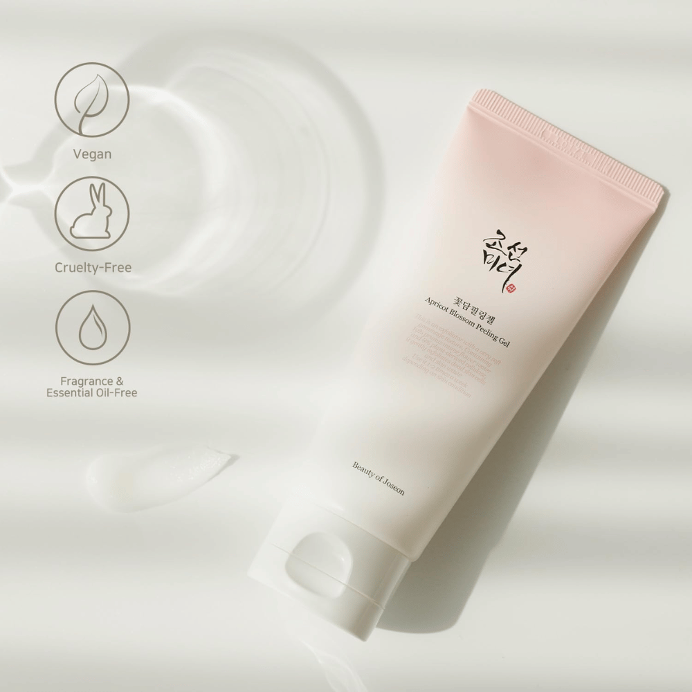 Eine Tube mit Apricot Blossom Peeling Gel liegt auf einer reflektierenden Oberfläche mit Symbolen, die angeben, dass das Produkt vegan, tierfreundlich und frei von Duft- und ätherischen Ölen ist.