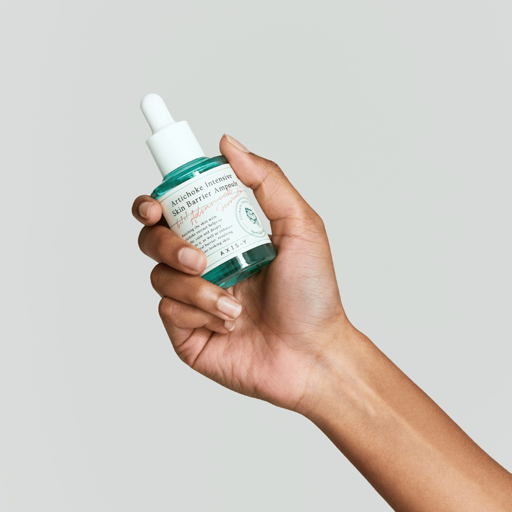 Eine Hand hält eine Flasche Hautpflegeserum mit dem Etikett "Artichoke Intensive Skin Barrier Ampoule.
