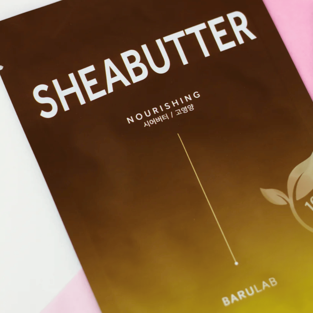 Eine Nahaufnahme einer Verpackung der BARULAB "SHEABUTTER Nourishing" Maske. Das Produkt ist als "100% Vegan Product" gekennzeichnet und hat einen Farbverlauf von Dunkelbraun zu Hellbraun.