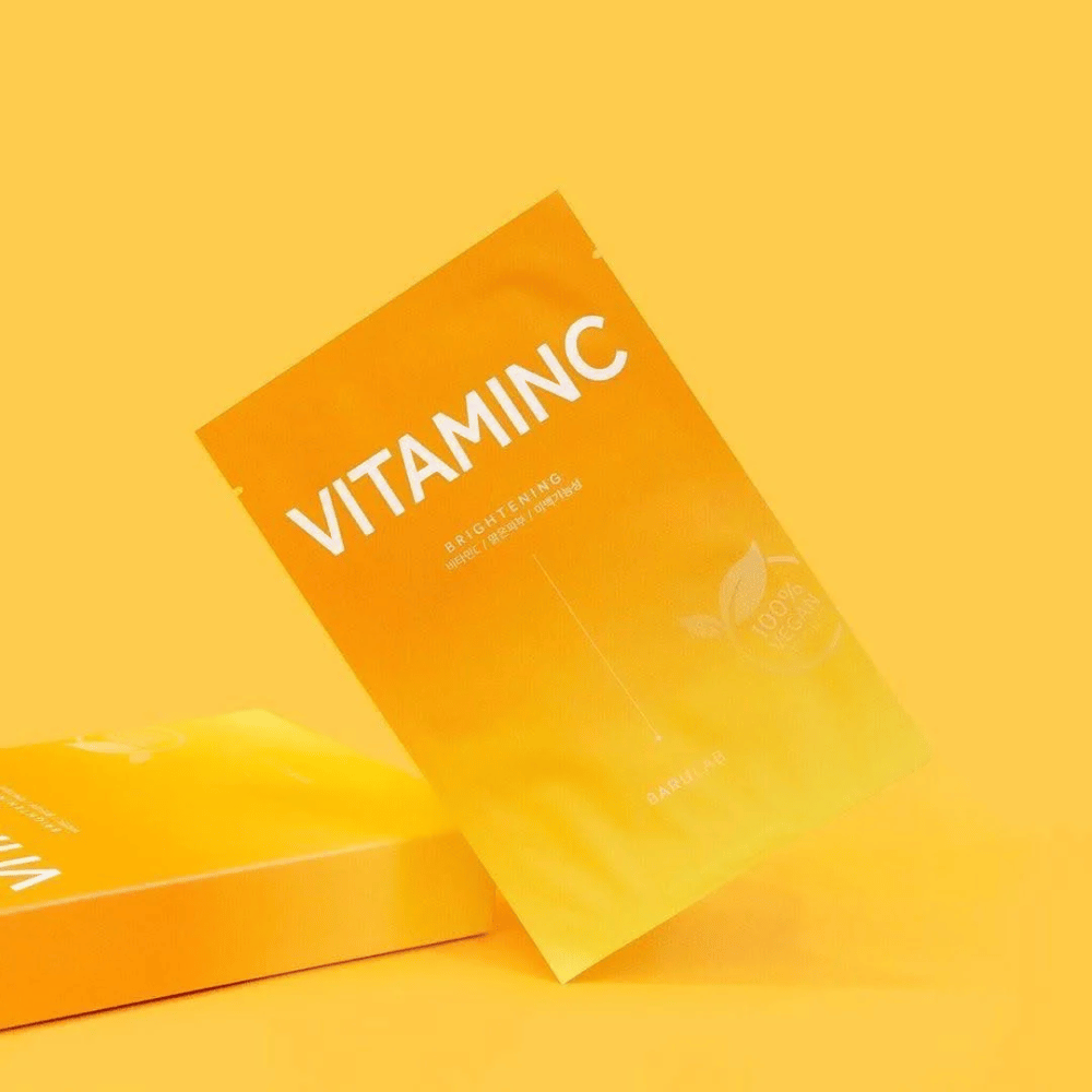 Ein Stapel von Verpackungen von BARULAB "VITAMINC Brightening" Masken, alle gekennzeichnet als "100% Vegan Product". Die Verpackungen haben eine Farbton in verschiedenen Schattierungen von Orange und Gelb, platziert vor einem einheitlichen gelben Hintergrund.