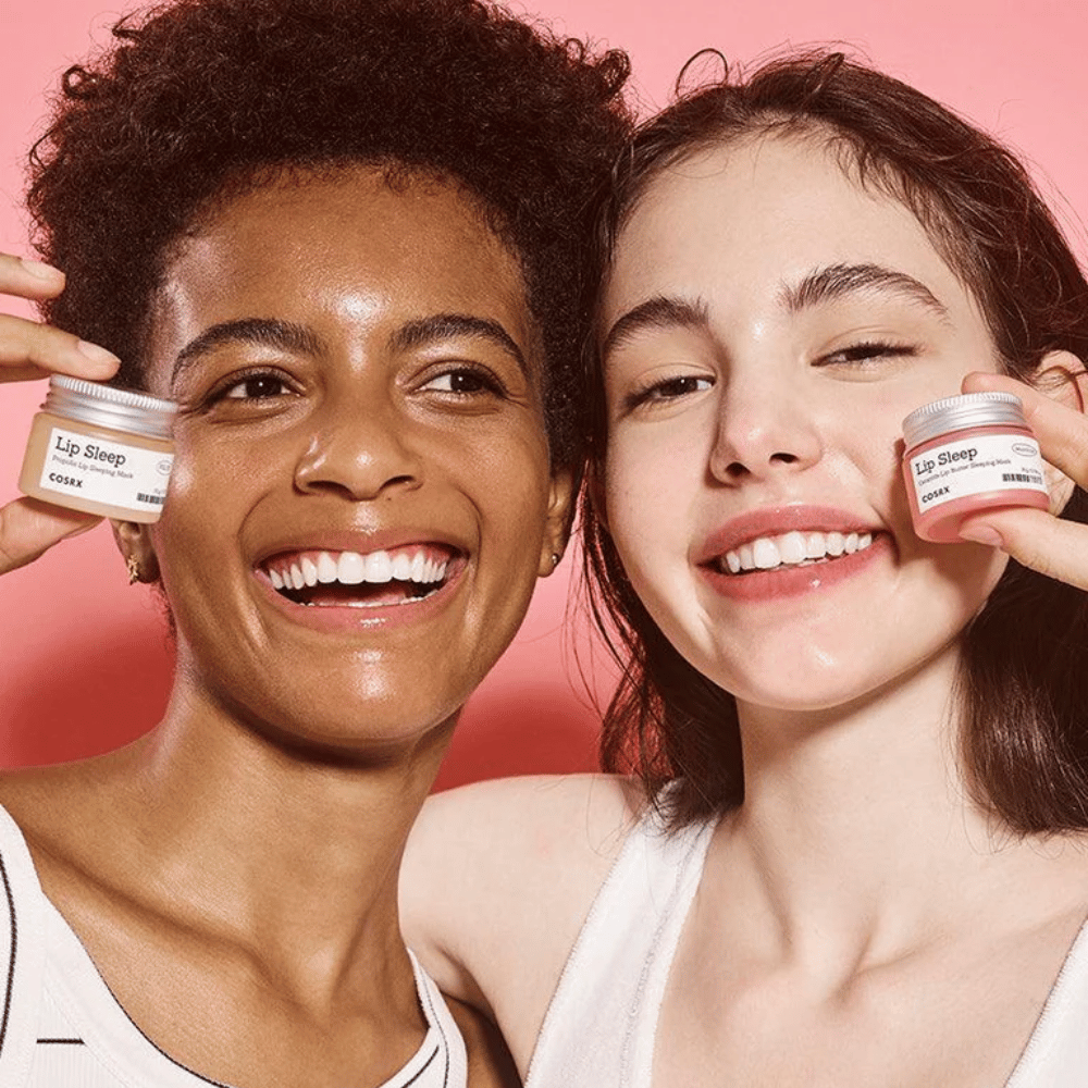 Zwei Personen lächeln und halten COSRX Lip Sleep-Tiegel hoch. Das Bild vermittelt weiche, mit Feuchtigkeit versorgte Lippen und den natürlichen Glow-Effekt des Produkts.