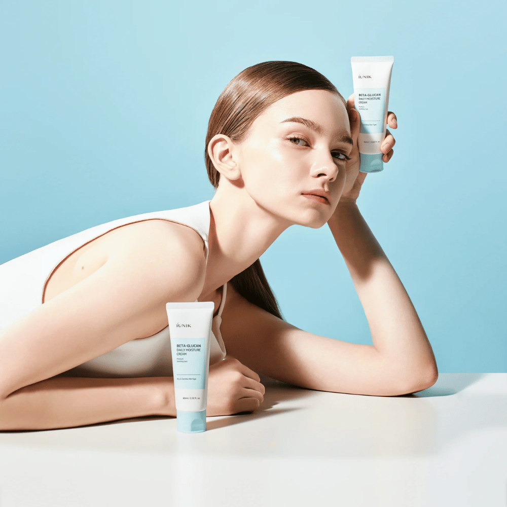 Lifestyle-Bild, auf dem ein Model mit iUNIK Beta-Glucan Daily Moisture Cream vor einem hellblauen Hintergrund posiert. Das Bild vermittelt ein sauberes, frisches und feuchtigkeitsspendendes Gefühl, während das Produkt deutlich präsentiert wird.