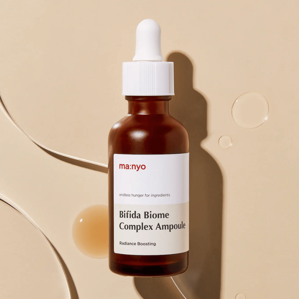 Stilvolles Produktbild von ma:nyo Bifida Biome Complex Ampoule mit Fokus auf Flaschendesign und Serumtropfen im Hintergrund.