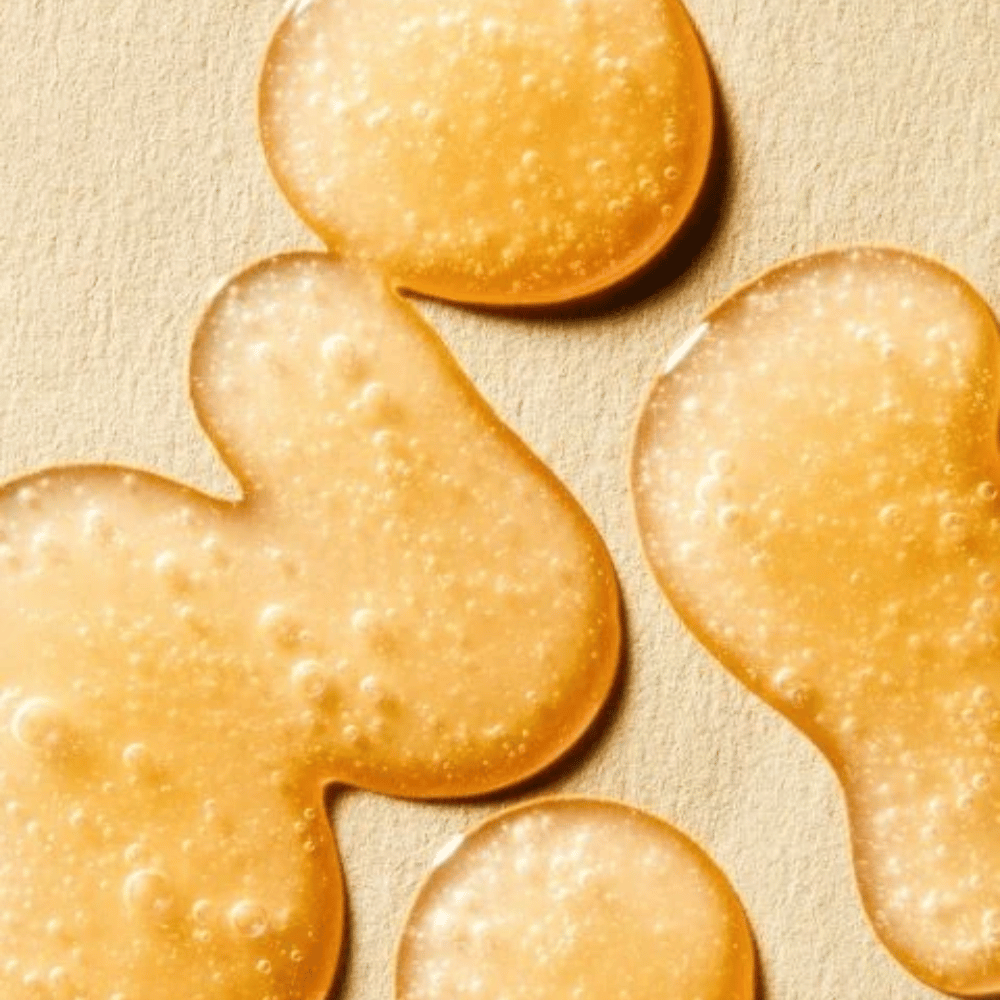 Texturbild, das die goldene Formel des Serums mit kleinen Bläschen und leicht gelartiger Konsistenz zeigt.