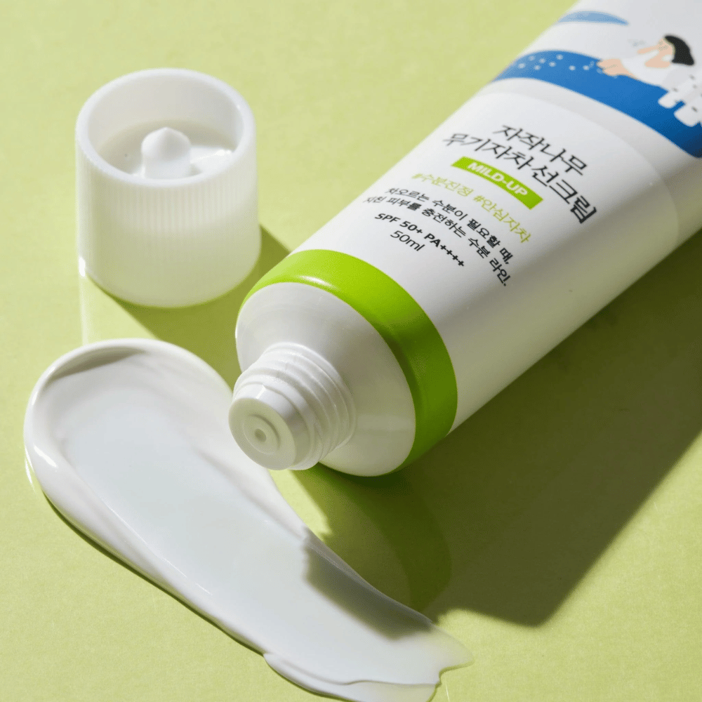 Nahaufnahme von Birch Juice Moisturizing Mild Up Sunscreen mit abgeschraubtem Deckel, weiße Sonnencreme verschmiert auf hellgrünem Hintergrund, SPF 50+ PA++++, 50 ml.