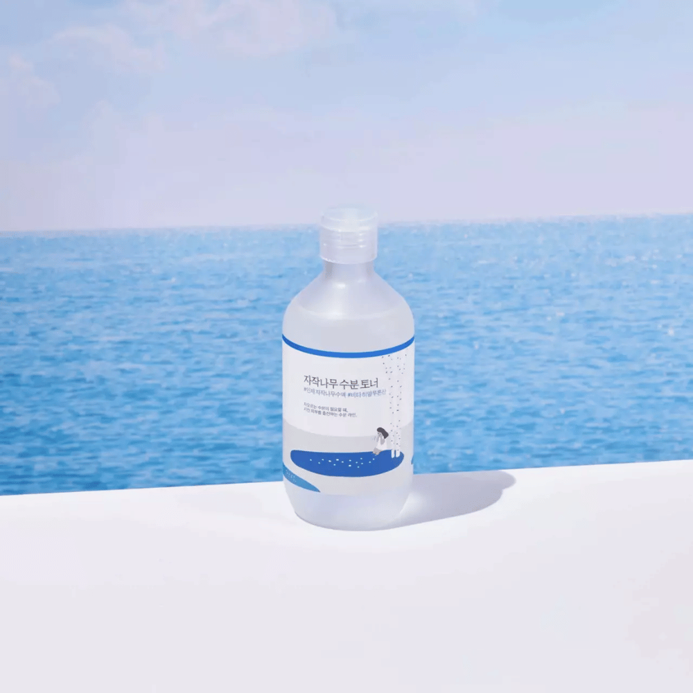 Flasche von ROUND LAB Birch Juice Moisturizing Toner steht auf einer weißen Fläche mit Meer und blauem Himmel im Hintergrund