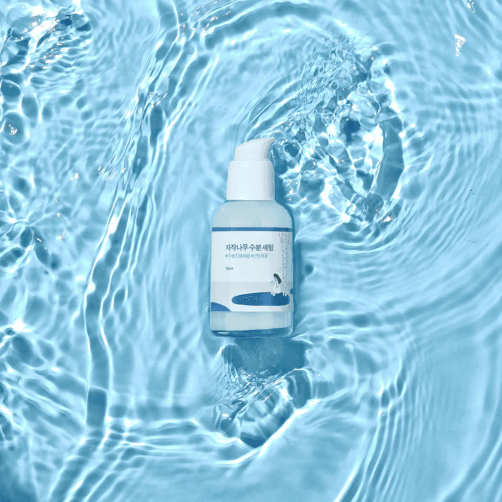 Round Lab Birch Juice Moisturizing Serum in Pumpflasche schwimmend auf blauem Wasser mit Sonnenlichtreflexionen.