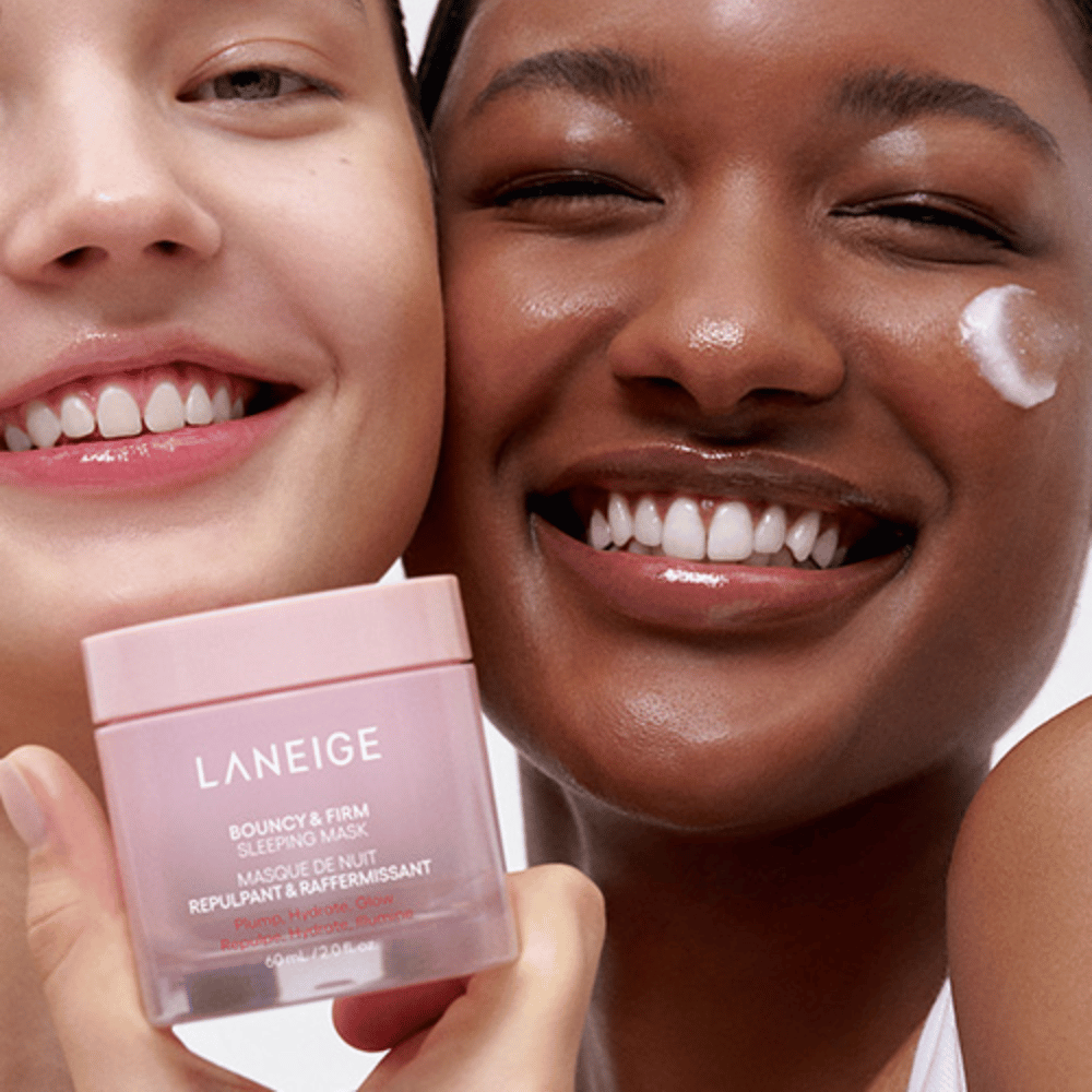 Zwei Personen lächeln und halten Laneige Bouncy & Firm Sleeping Mask. Eine hat die Maske auf ihre Wange aufgetragen, und das Produkt ist deutlich in ihren Händen sichtbar. Die Maske ist in einem rosa Glasgefäß und wird als "Plump, Hydrate, Glow" vermarktet.
