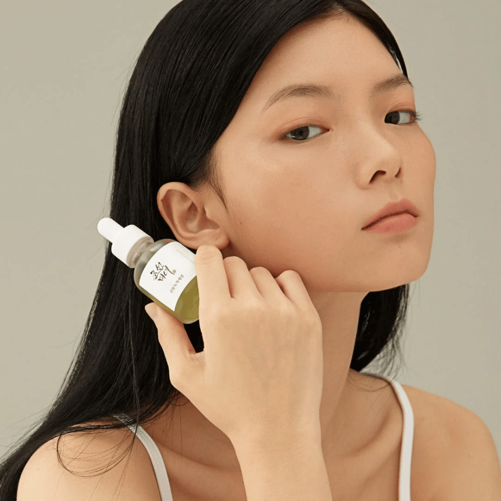 Modell hält Beauty of Joseon Calming Serum an der Wange – grüner Tee und Panthenol, das die Hautbarriere stärkt.