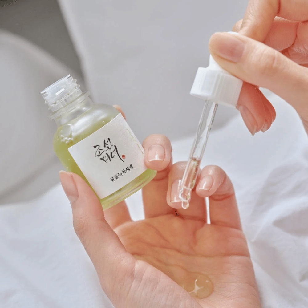 Hand tropft Beauty of Joseon Calming Serum Green Tea + Panthenol auf die Haut – beruhigendes koreanisches Serum für empfindliche Haut.