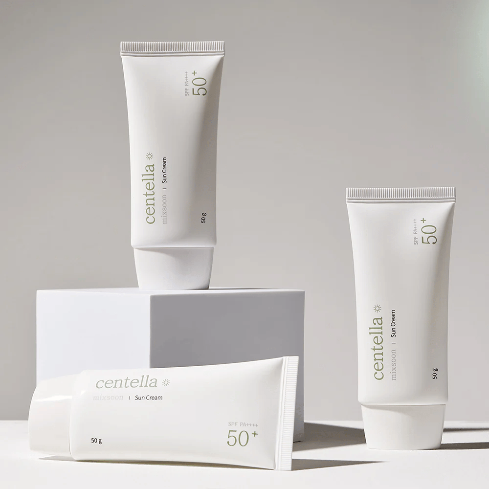 Drei Packungen Centella Sun Cream SPF 50+ PA++++ ästhetisch auf weißen Podesten angeordnet. Zwei Tuben stehen aufrecht und eine liegt, alle mit weißem, minimalistischem Design und grünen Textdetails.