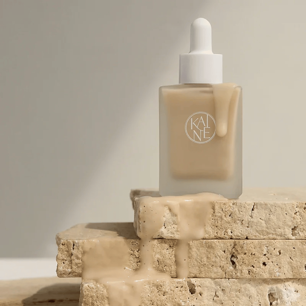 KANE Chaga Collagen Charging Serum in einer mattierten Glasflasche mit Pipette. Cremige Textur fließt über natürliche Steine in einem sanften und minimalistischen Licht.