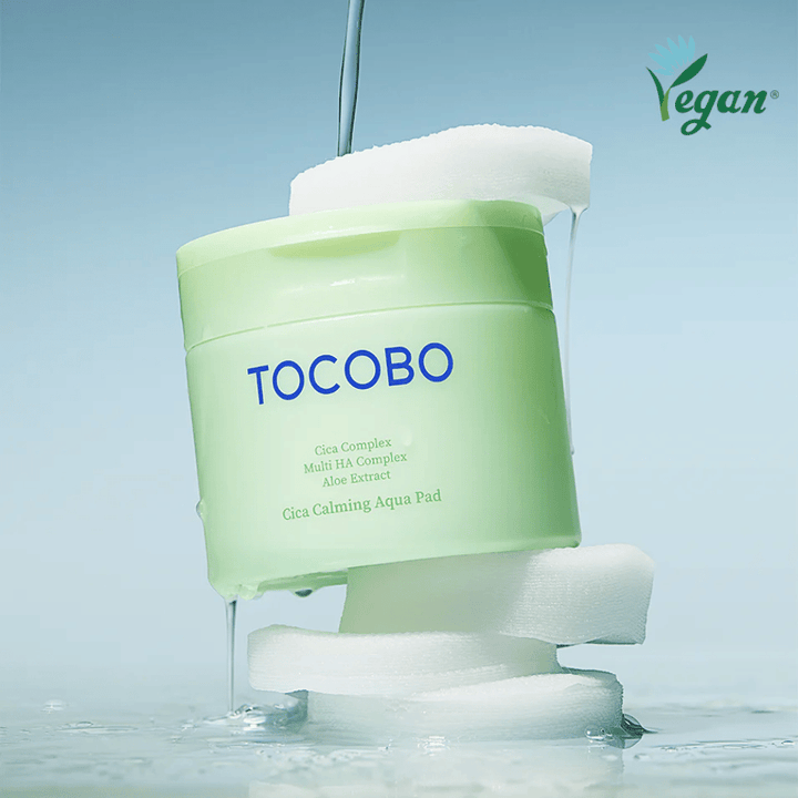 TOCOBO Cica Calming Aqua Pad zwischen toner pads mit fließender Essenz platziert. Das Vegan-Symbol betont die vegane Formulierung des Produkts und sein hautfreundliches Profil.