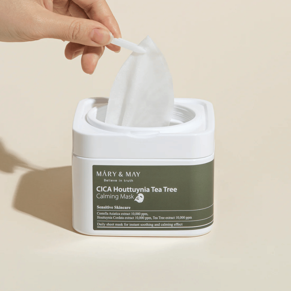 Hand, die eine Sheet-Maske aus der Mary & May Cica Houttuynia Tea Tree Calming Mask-Dose zieht – beruhigende Gesichtsmaske für empfindliche Haut mit Cica und Tea Tree-Extrakt.
