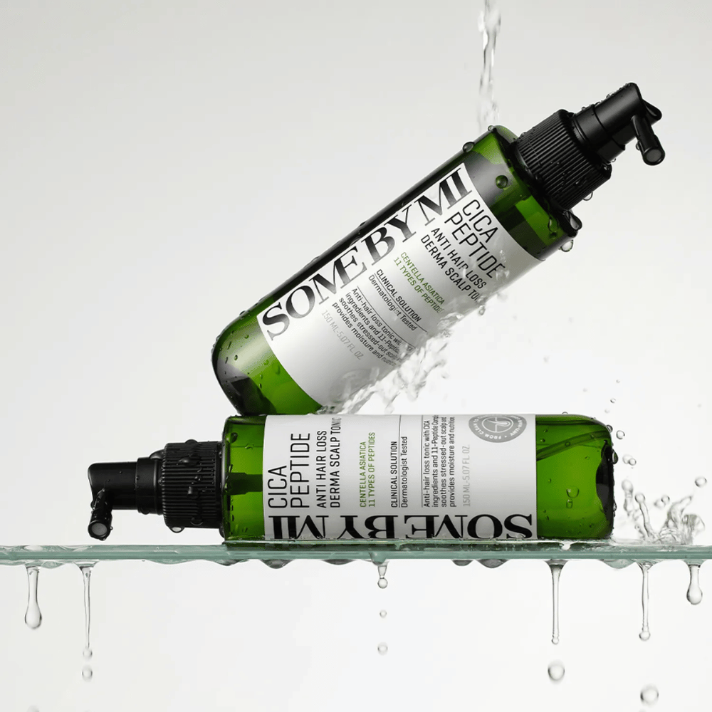Zwei Flaschen SOME BY MI Cica Peptide Anti Hair Loss Derma Scalp Tonic liegen im und über dem Wasser mit spritzenden Tropfen, grüne Flaschen mit schwarzem Sprühkopf und weißem Etikett.