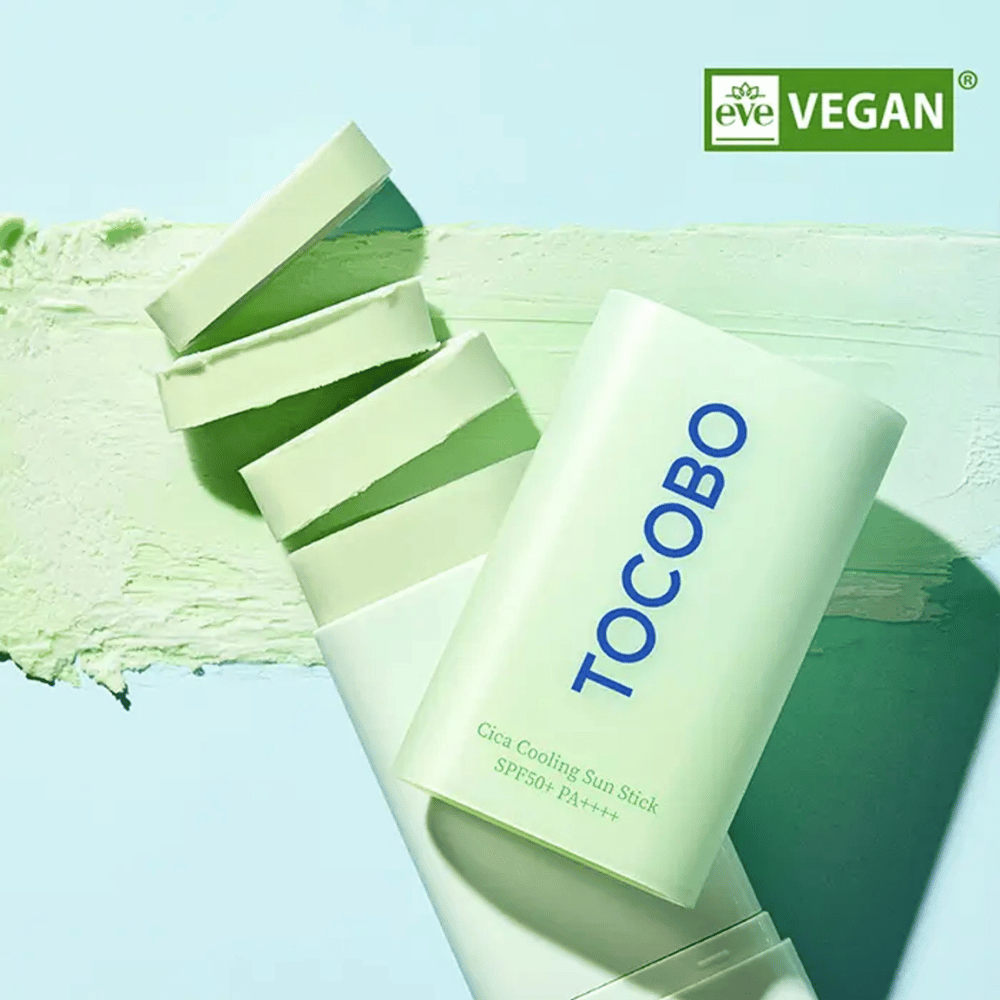 Tocobo Cica Cooling Sun Stick SPF50+ PA++++ in hellgrüner Verpackung mit Vegan-Zertifizierung (EVE VEGAN), liegend auf einer Schicht aus grünem Sonnenstift.