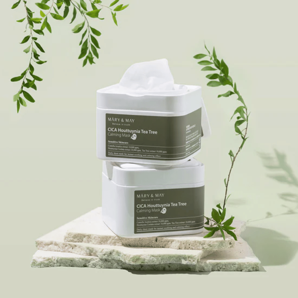 Zwei Dosen Mary & May Cica Houttuynia Tea Tree Calming Mask auf Naturstein mit grünen Pflanzendetails platziert – beruhigende Sheet-Masken für empfindliche Haut.