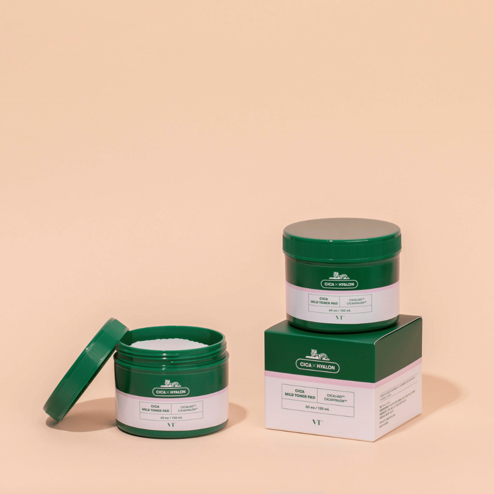 Zwei grüne Dosen mit VT Cica Mild Toner Pad, eine offene, die die weißen Tonerpads zeigt, und eine geschlossene, die auf ihrer Produktverpackung platziert ist, vor beigem Hintergrund.