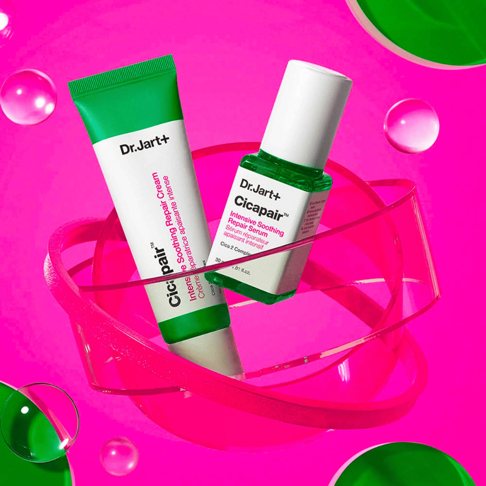 Dr.Jart+ Cicapair Intensive Soothing Repair Cream und Serum in grünen Verpackungen, die auf einer rosa kreisförmigen Basis stehen. Die Produkte sind entwickelt, um gereizte Haut zu beruhigen und zu reparieren.