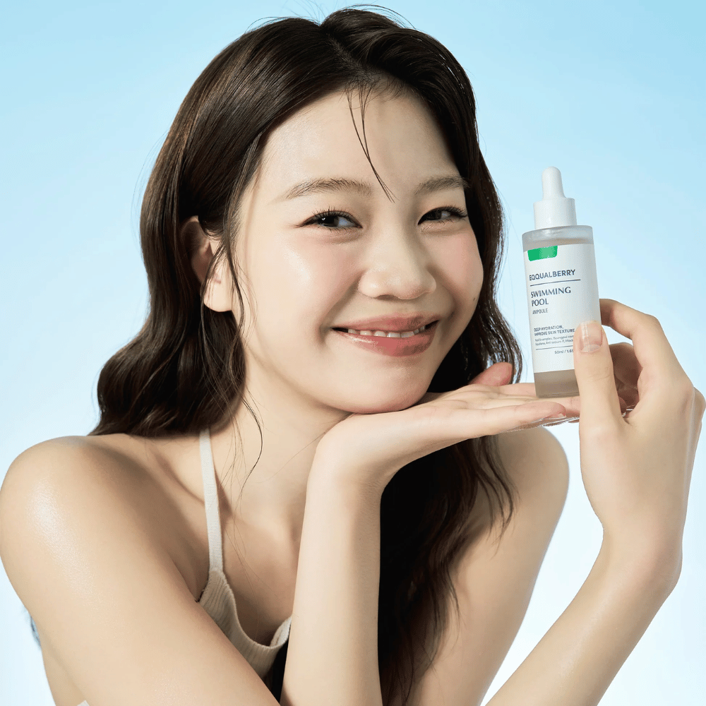Lächelnde Frau, die Eqqualberry Swimming Pool Ampoule, ein feuchtigkeitsspendendes Hautpflegeprodukt, mit beiden Händen vor einem hellblauen Hintergrund hält.