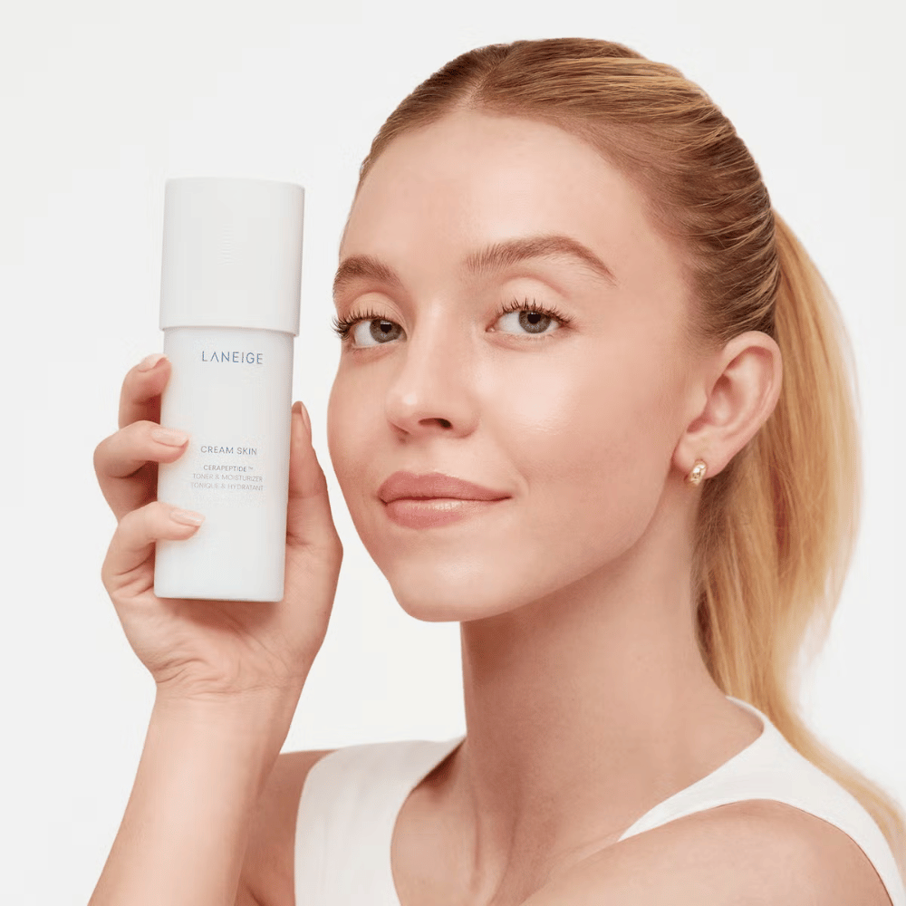 Eine Person hält Laneige Cream Skin Cerapeptide Refiner in einer weißen Flasche hoch. Die Person lächelt und zeigt das Produkt, das als feuchtigkeitsspendender Toner und Hautpflegeprodukt vermarktet wird.