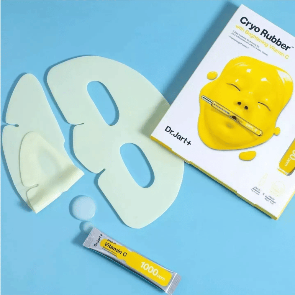 Bild von Dr.Jart+'s 'Cryo Rubber™ mit aufhellendem Vitamin C' Schönheitsprodukt. Vor einem blauen Hintergrund sieht man eine weiße Gummigesichtsmaske, eine kleine Tube mit der Aufschrift 'Vitamin C 1000ppm' und eine Schachtel mit dem Produktnamen und einem Bild der gelben Maske.
