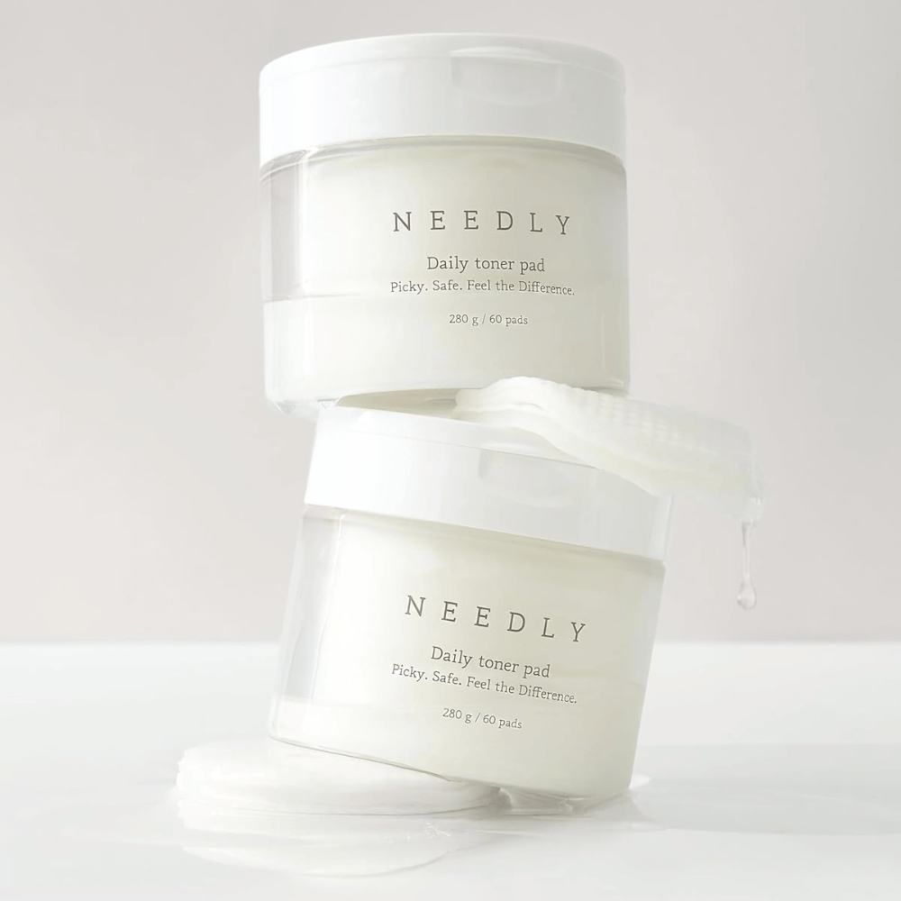 Zwei Behälter mit Needly Daily Toner Pad aufeinander gestapelt. Die Behälter sind weiß mit minimalistischem Text und enthalten jeweils 60 Tonerpads. Ein Tonerpad liegt teilweise außerhalb des oberen Behälters mit Flüssigkeit, die abtropft.