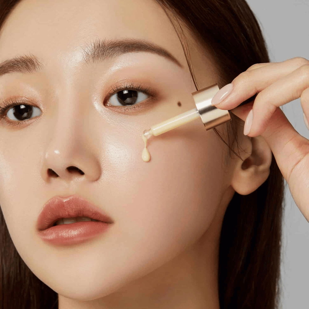 Nahaufnahme einer Frau, die Medicube Deep Vita C Ampoule mit einer goldfarbenen Pipette aufträgt. Ein Tropfen des Serums ist dabei, ihre Haut zu erreichen, die einen natürlichen Glanz hat. Perfekt, um einen helleren und gleichmäßigeren Hautton zu erzielen.