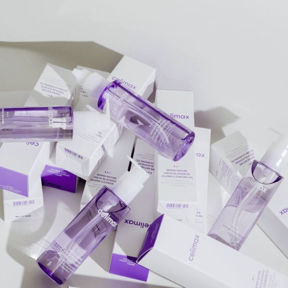 Celimax Derma Nature Fresh Blackhead Jojoba Cleansing Oil in lila Flaschen, platziert zwischen weißen Produktverpackungen mit lila Details.