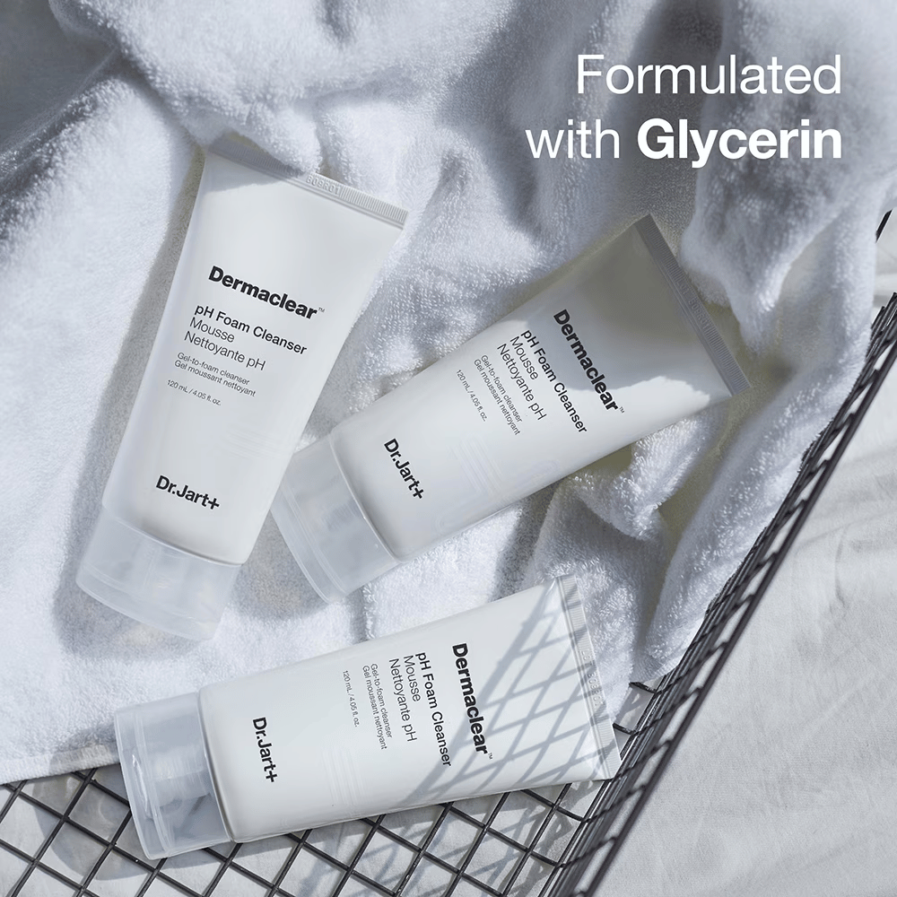 Drei Tuben von Dr.Jart+ Dermaclear pH Foam Cleanser liegen auf einem weißen Frotteehandtuch in einem Metallkorb, mit dem Text "Formulated with Glycerin" in der oberen Ecke.