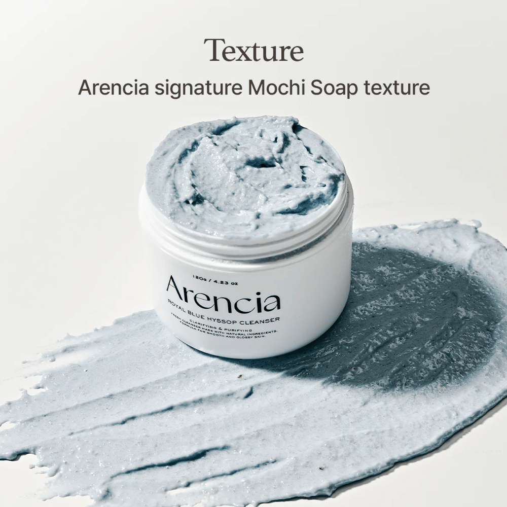Offenes Glas mit Arencia Fresh Blue Hyssop Rice Mochi Cleanser, platziert auf einer verschmierten Schicht der blauen, cremigen Reinigungsformel, die ihre mochi-ähnliche Textur zeigt.