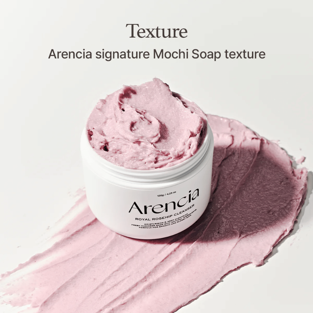Burk med Arencia Royal Rosehip Cleanser syns ovanpå en utsmetad rosa rengöring med mochi-liknande textur. Texten ovanför beskriver produkten som Arencias signaturtextur.
