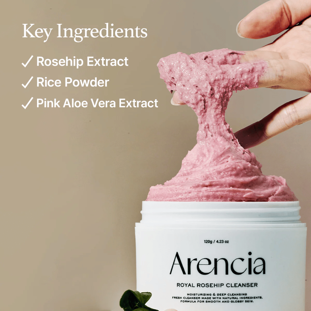 Eine Hand hebt die rosa, flauschige Reinigungstextur aus dem Behälter Arencia Royal Rosehip Cleanser, mit Zutatenliste links: Hagebuttenextrakt, Reispulver und rosa Aloe Vera-Extrakt.