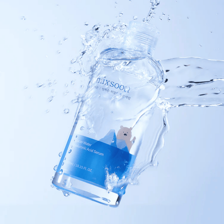 Mixsoon Glacier Water Hyaluronic Acid Serum-flaska med blå etikett och isbjörnsmotiv omgiven av skvättande vatten mot ljusblå bakgrund.