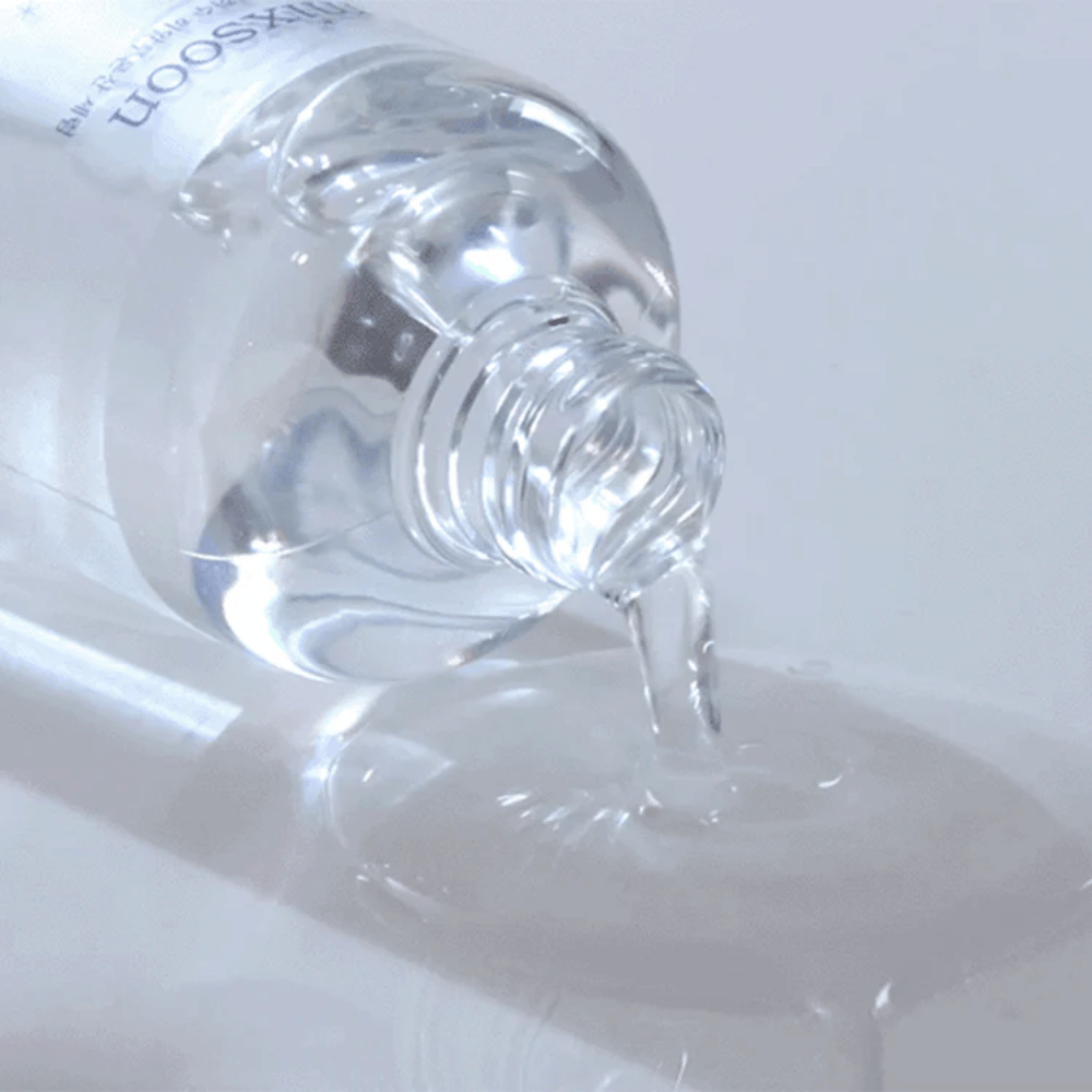 Nahaufnahme von durchsichtigem Serum, das aus einer Flasche Mixsoon Glacier Water Hyaluronic Acid Serum auf eine glänzende Oberfläche gegossen wird.