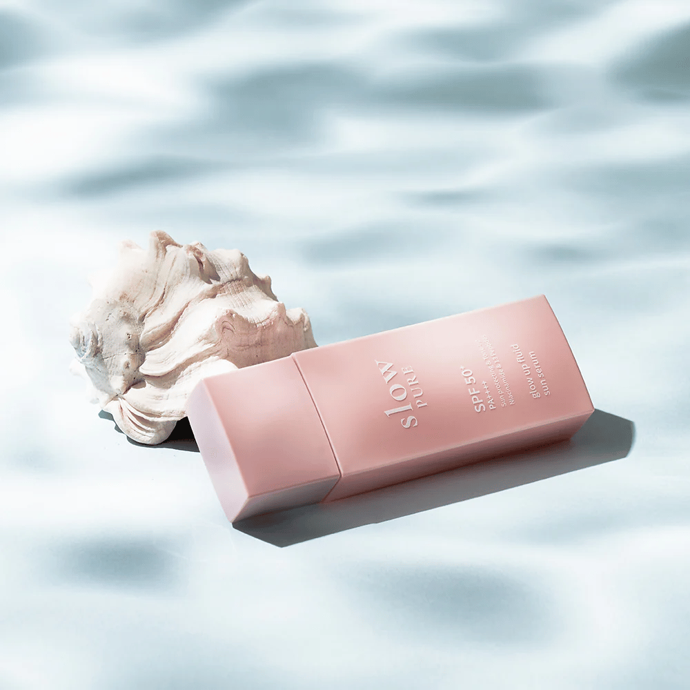 Slow Pure Glow Up Fluid Sun Serum bei Muschelschale und Wassereffekt, hebt Sonnenschutz und Strahlkraft hervor.