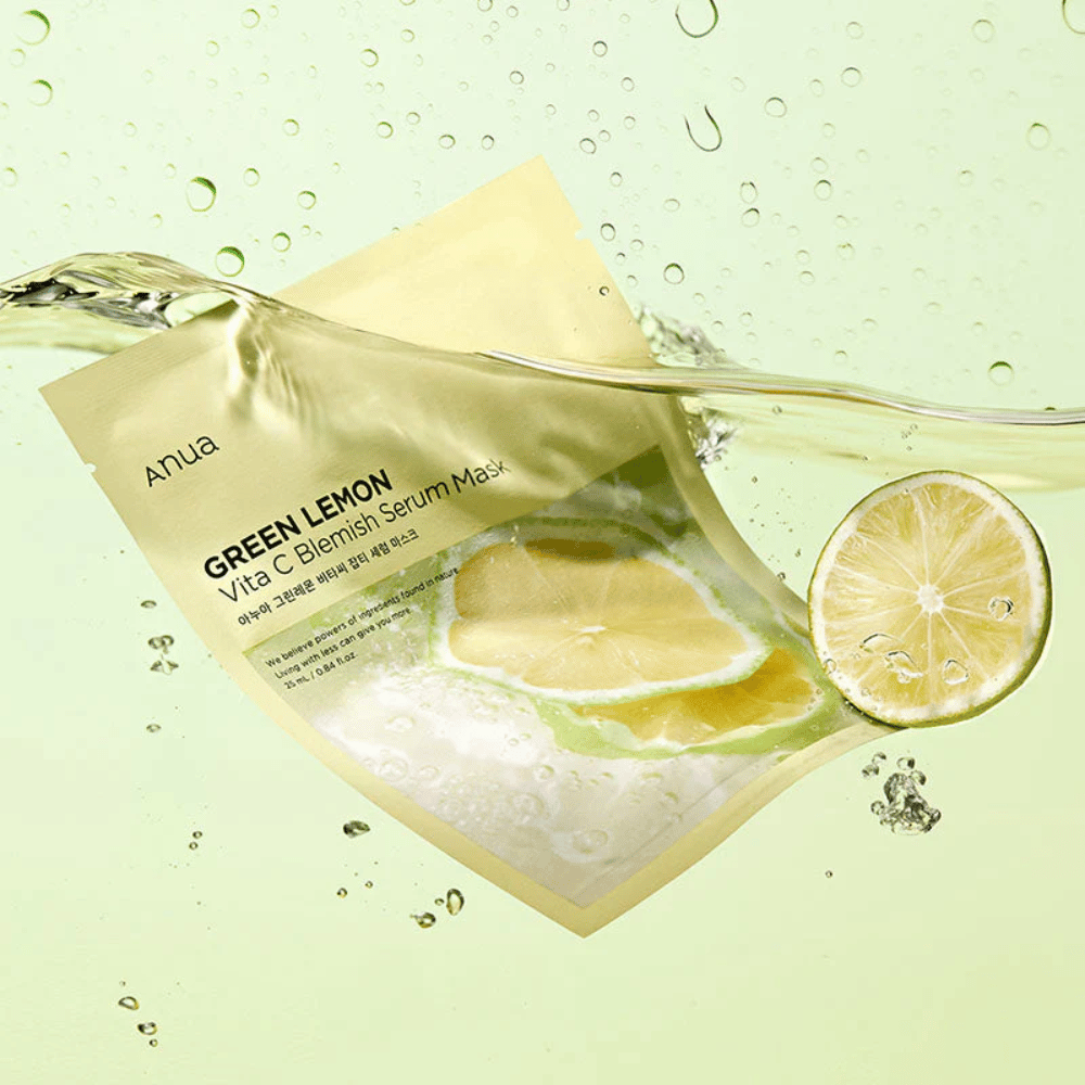 Ein lebendiges Bild der Anua Green Lemon Vita C Blemish Serum Mask Verpackung mit durchsichtigen Wassertropfen und Scheiben von grüner Zitrone rundherum. Die Verpackung ist teilweise von einem Wasserstrom auf einem hellgrünen Hintergrund bedeckt.