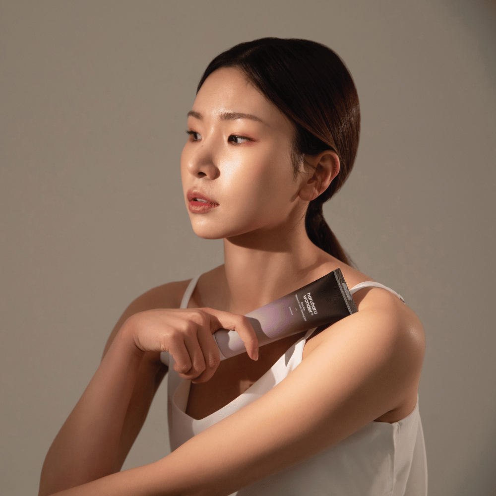Eine junge asiatische Frau, die eine Bürste in der Hand hält, während sie Haruharu Wonders Black Rice Moisture 5.5 Soft Cleansing Gel 100ml verwendet.