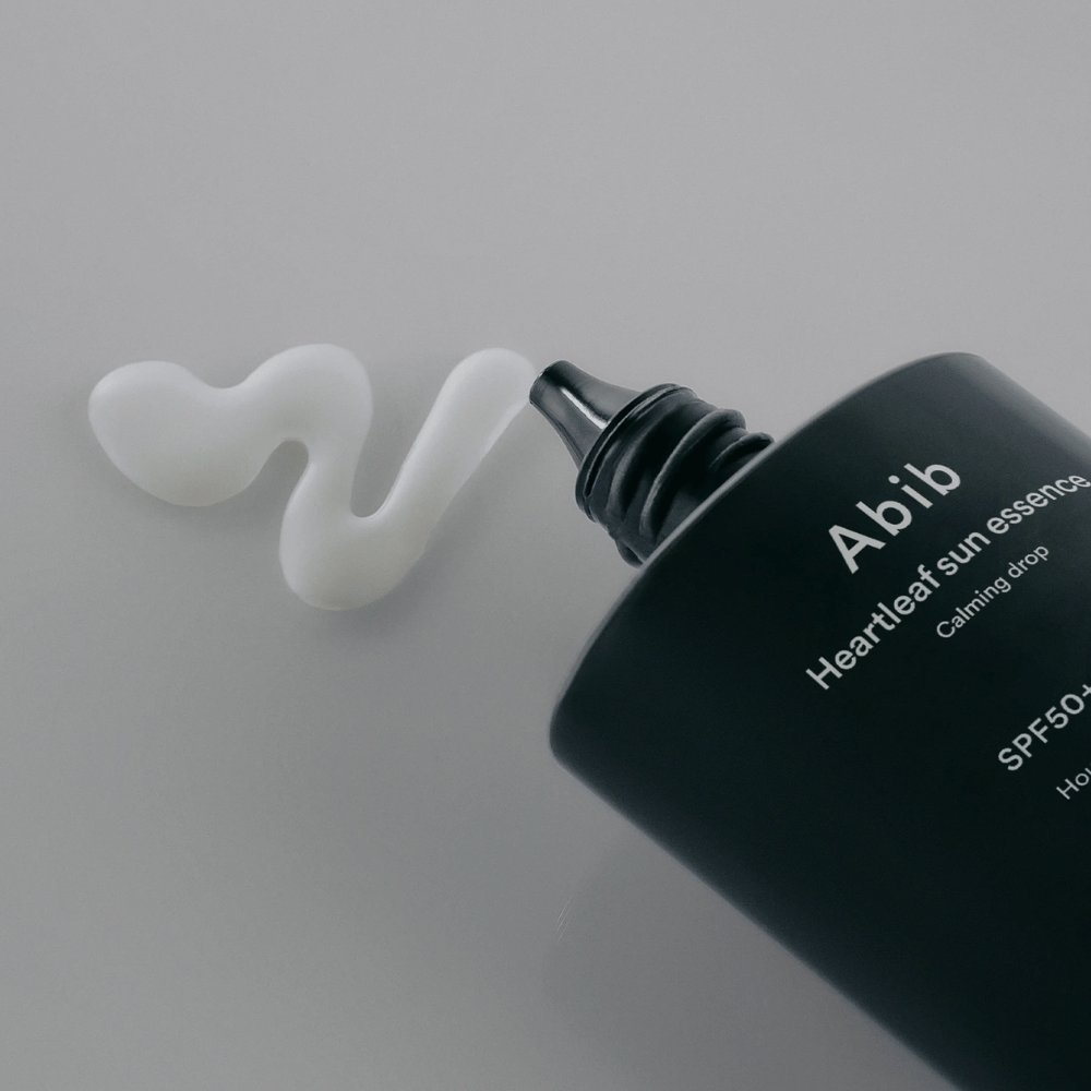 Nahaufnahme von Abib Heartleaf Sun Essence Calming Drop mit der Sonnencreme, die in einer weißen, welligen Linie auf einer hellen Oberfläche herausgedrückt ist.