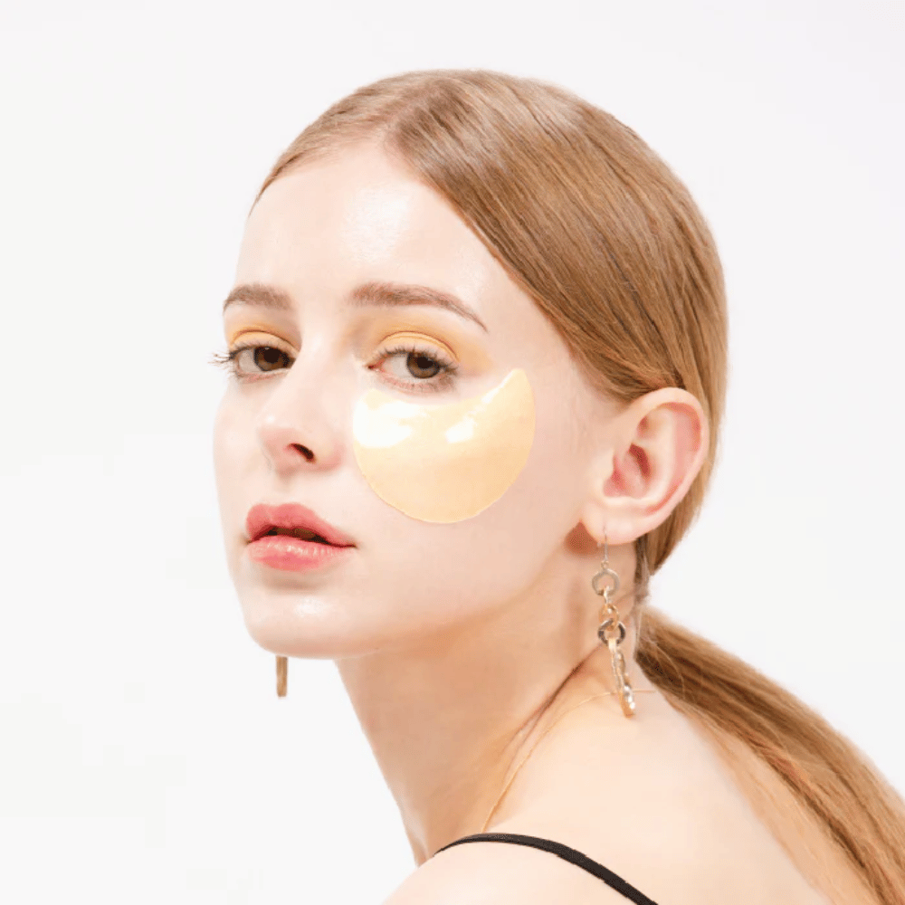 Modell trägt ein goldschimmerndes Hydrogel-Augenpflaster unter dem Auge für einen strahlenden Effekt.