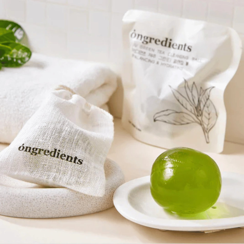 Óngredients Jeju Green Tea Cleansing Ball auf einem Teller mit Verpackung und Handtuch platziert – sanfte Reinigung mit grünem Tee aus Jeju.