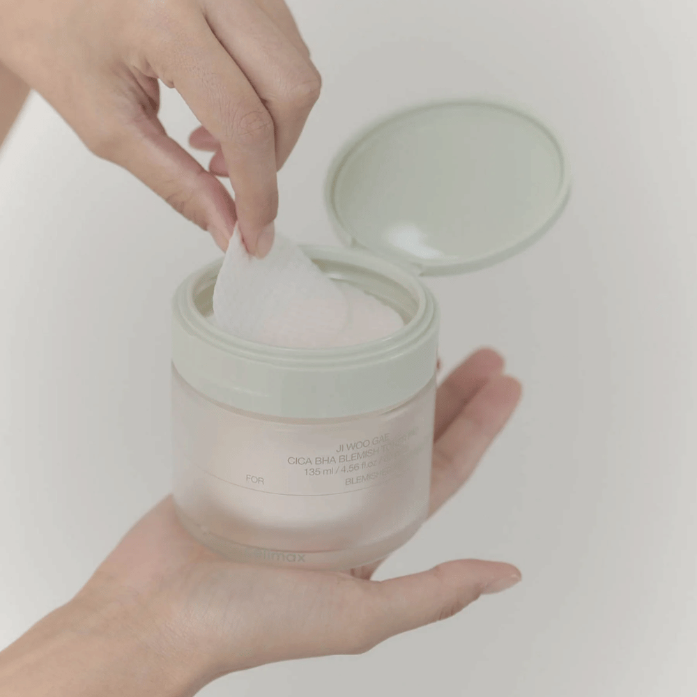 Hand nimmt ein Toner-Pad aus dem Glas Celimax Ji Woo Gae Cica BHA Blemish Toner Pad, perfekt für unreine Haut.