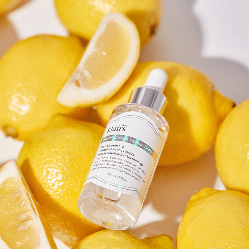 Klairs Freshly Juiced Vitamin Drop Serumflasche umgeben von frischen Zitronenhälften und Zitronenscheiben auf einer hellen Oberfläche, hebt die Zutaten hervor.