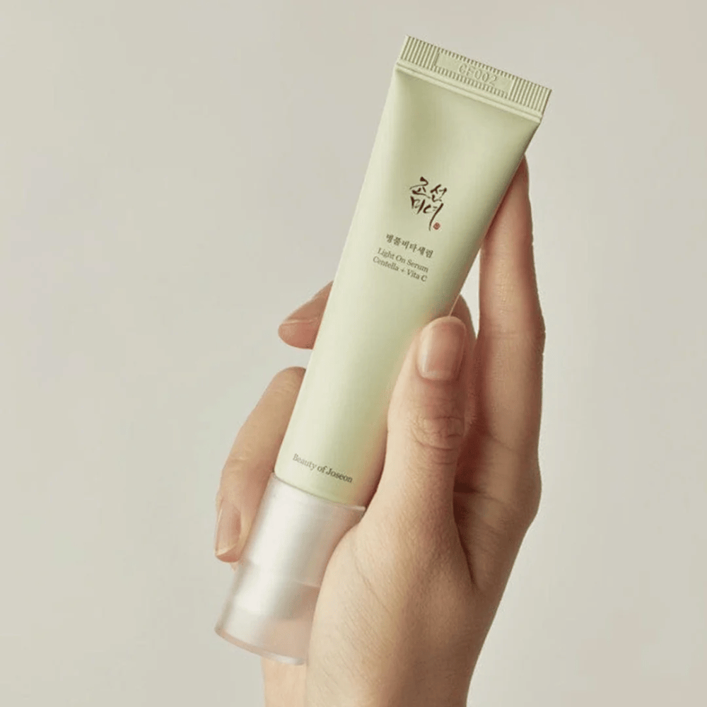 Eine Hand hält Beauty of Joseon Light On Serum mit Centella und Vitamin C, in einer hellgrünen Tube mit minimalistischem Design vor einem neutralen Hintergrund.