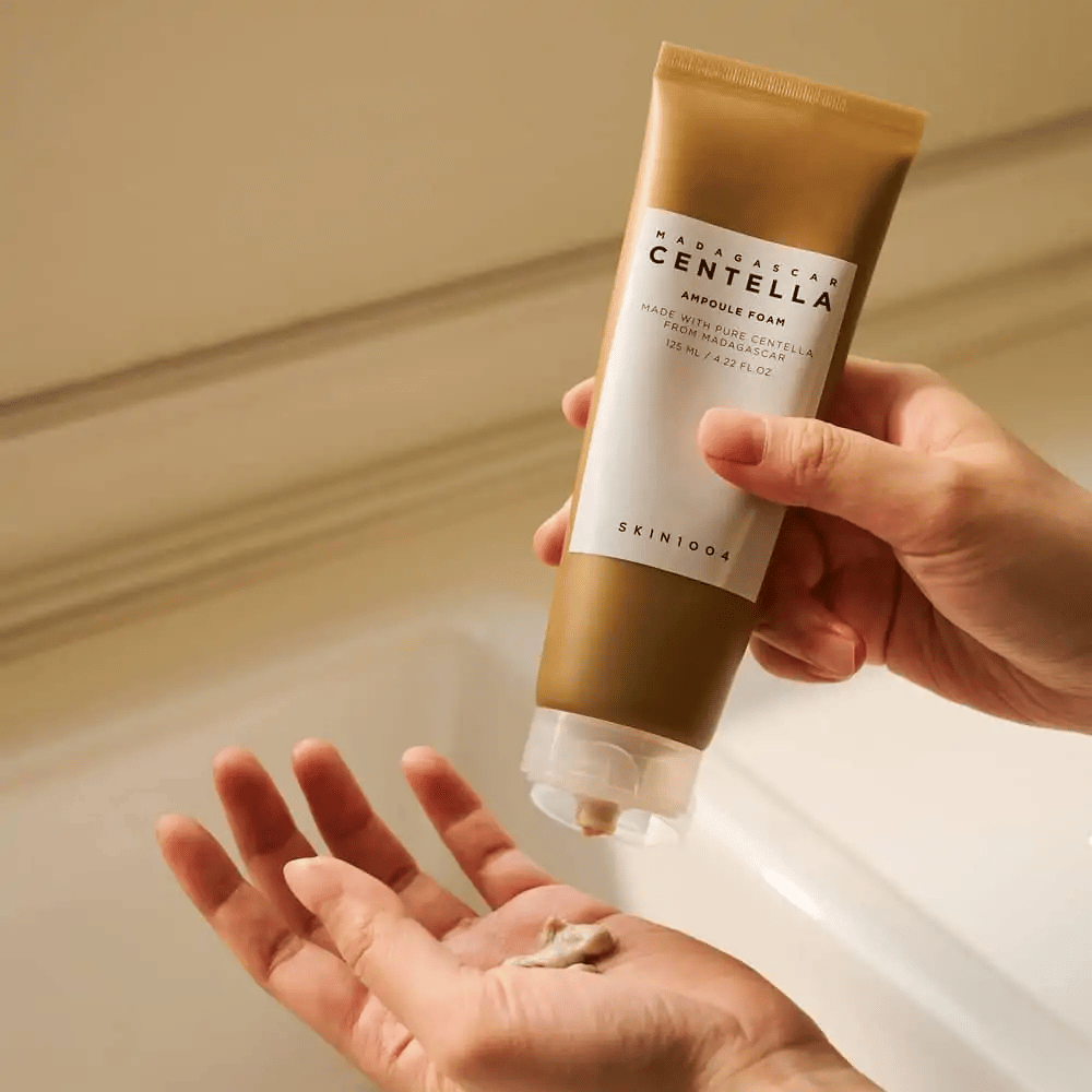 Das Produkt auf dem Bild ist "Madagascar Centella Ampoule Foam" von SKIN1004. Es ist eine Gesichtswäsche in Form eines Schaums, hergestellt aus Centella aus Madagaskar. Es enthält 125 ml / 4.22 fl.oz. Eine Hand drückt eine kleine Menge des Produkts zur Verwendung aus.