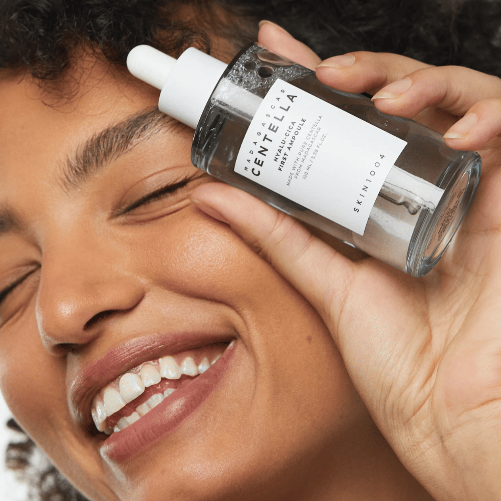 Lächelnde Frau hält Skin1004 Madagascar Centella Hyalu-Cica First Ampoule neben ihrem Gesicht hoch.